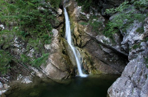 Manjsi slap, ki tece po skalnati steni, porasli z algami in mahom, obdan z drevesi.