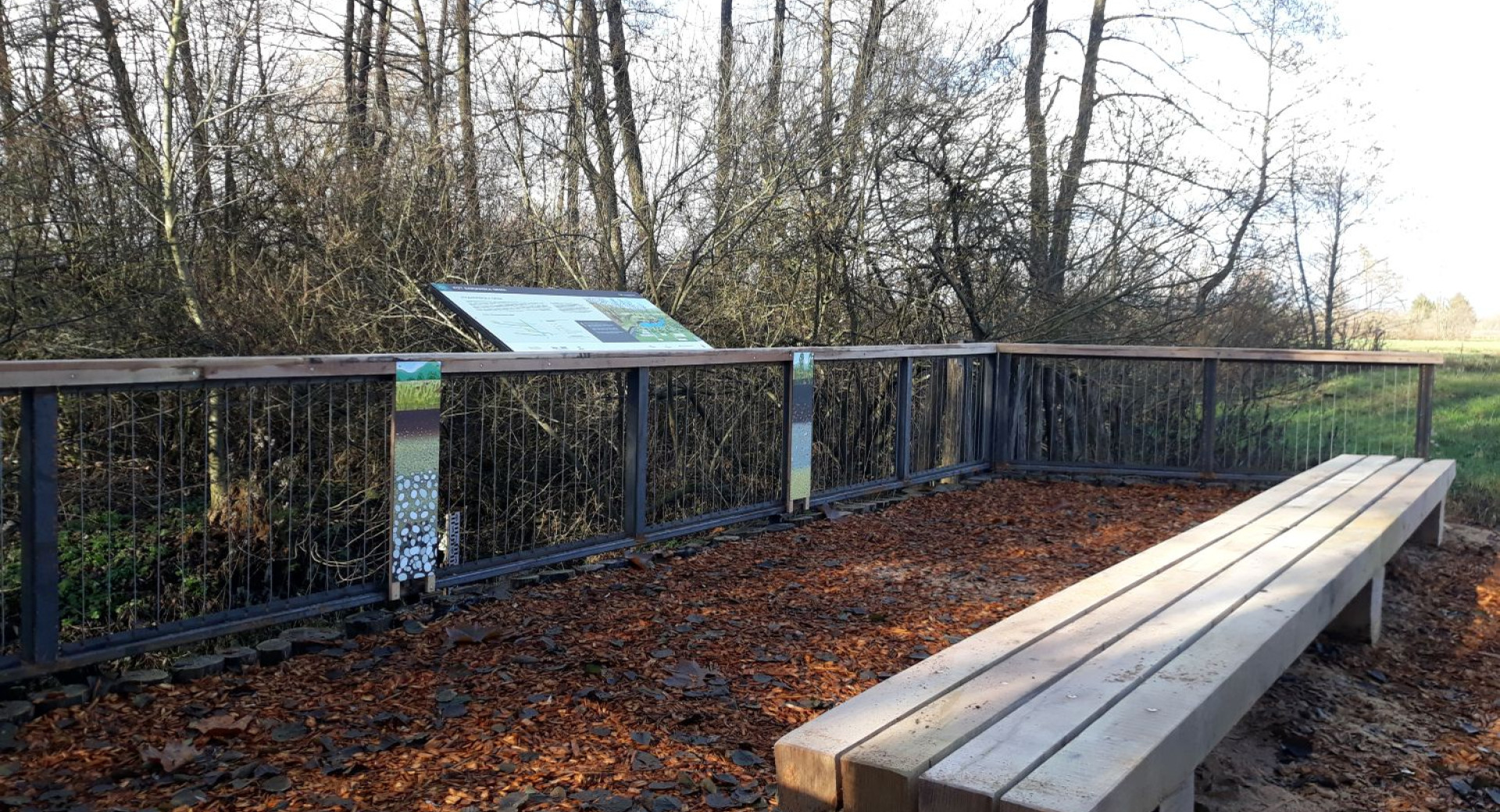 Klopica med jesenskim listjem z informativno tablo na bliznji ogradi. 