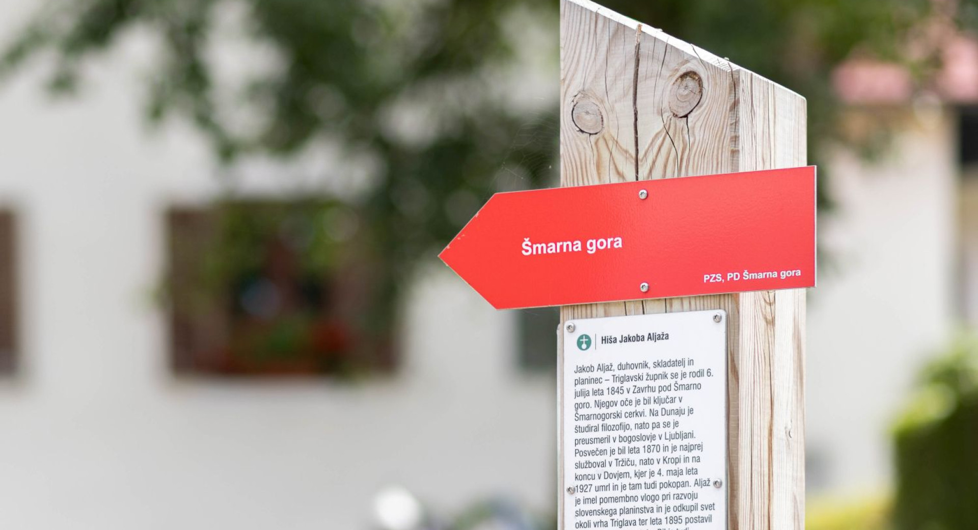 Ein rotes Schild mit der Aufschrift „Šmarna Gora“ auf einem Holzpfosten.