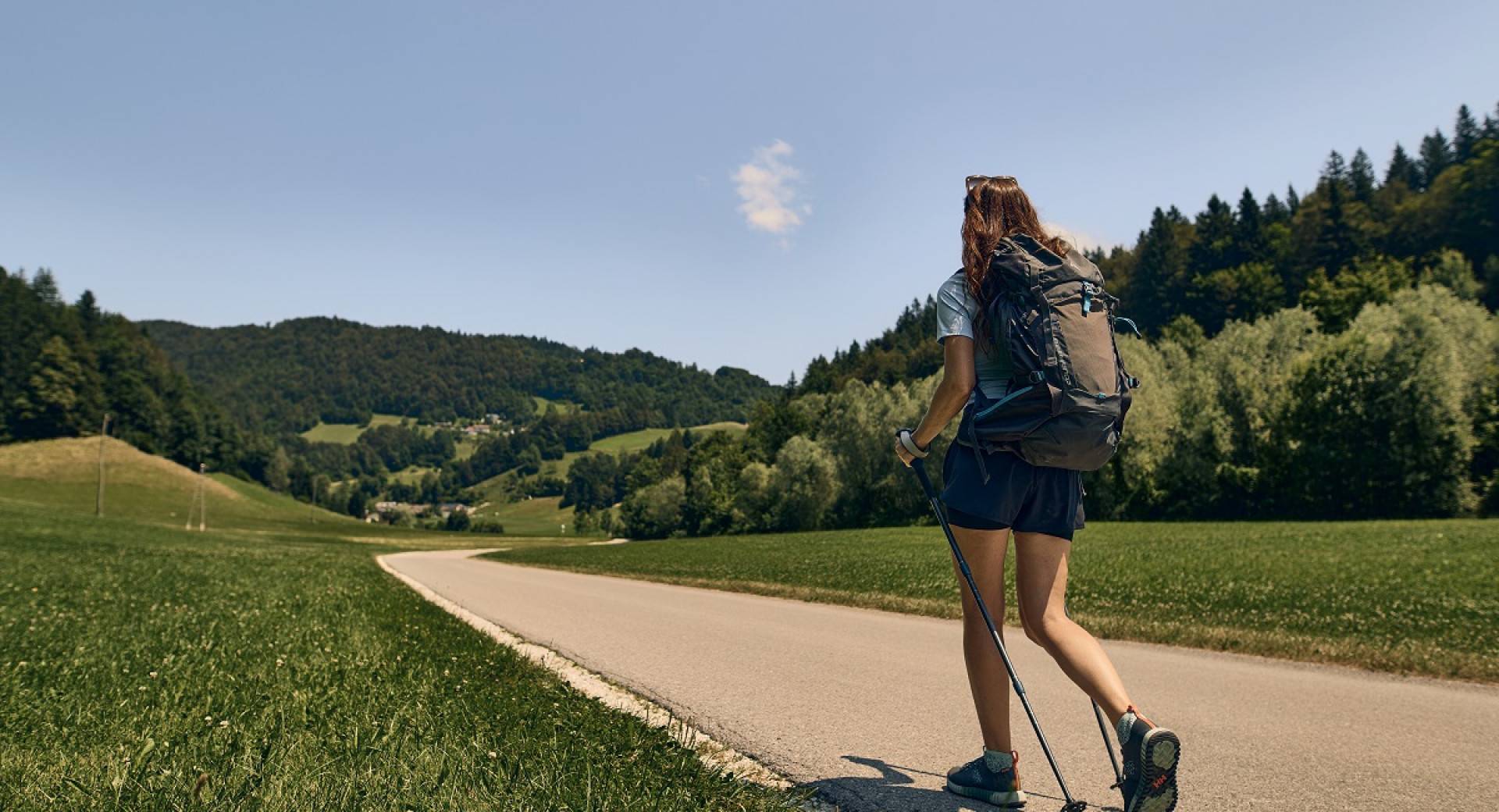 The hiker walks along the road through the rural landscape.
