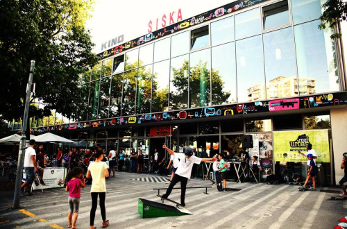 Decek rolka pred stekleno zgradbo-. Stavba z napisom 'Kino Siska'.