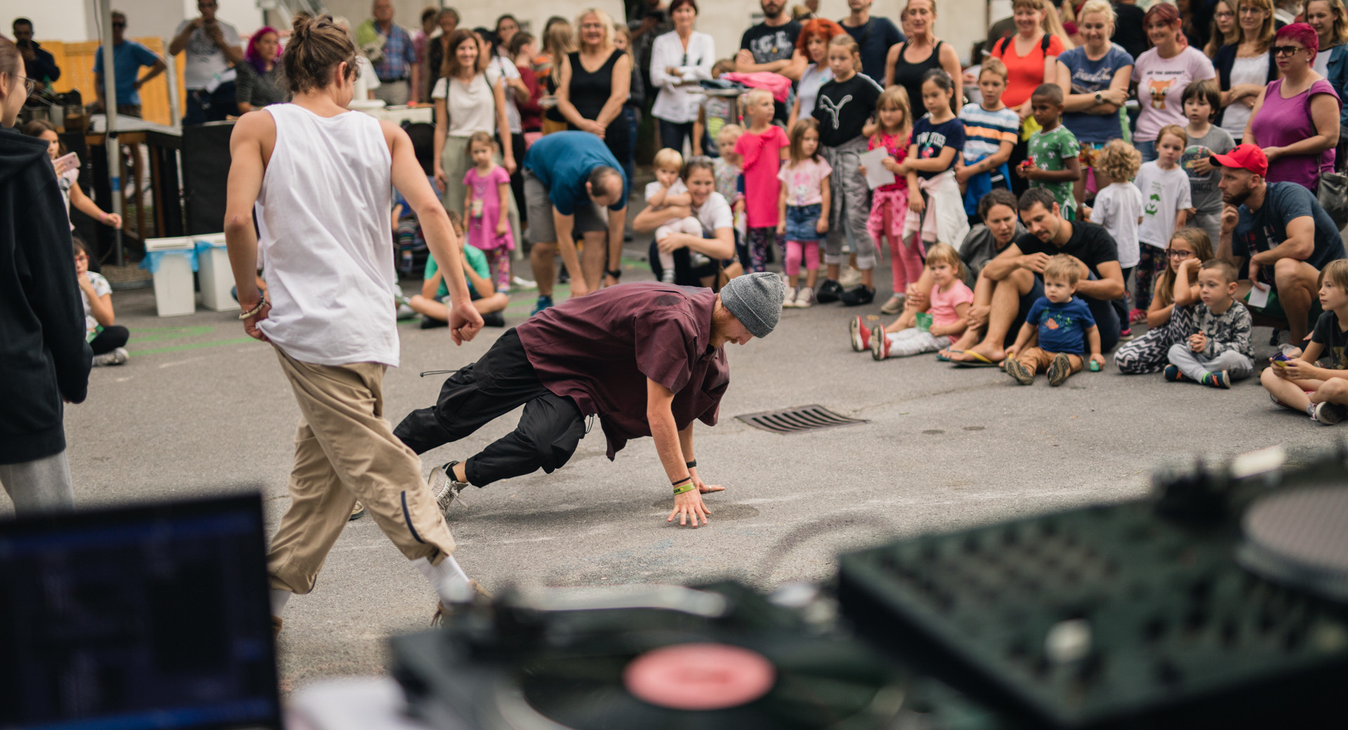 Ulicna breakdance predstava pred obcinstvom vseh generacij z DJ-jem in gramofonom na odprtem dogodku v mestnem okolju.