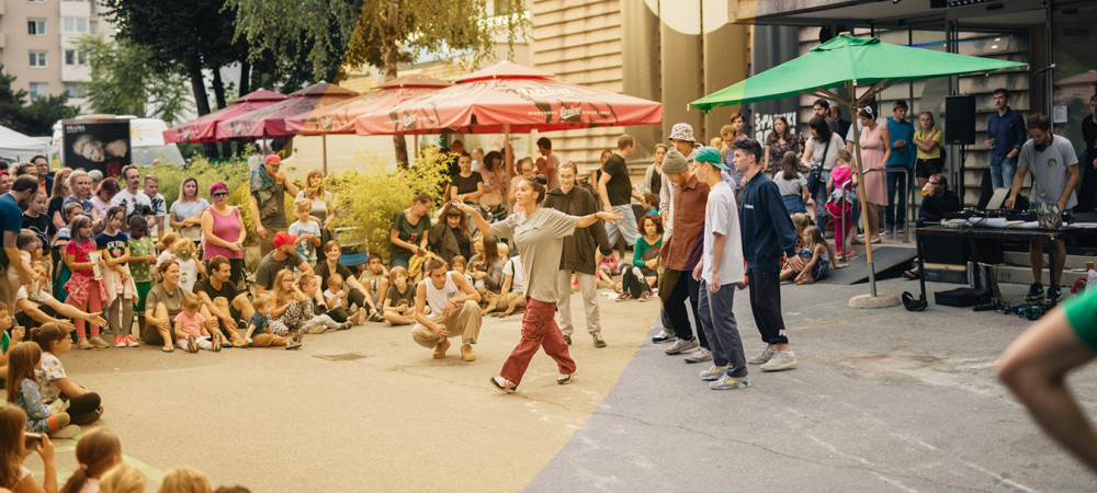 Performers are on the street in front of a building, surrounded by seated spectators.