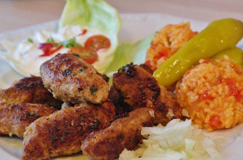 Na krozniku so pečeni cevapcici, riz z omako, kisli feferoni, nasekljana cebula in solata s smetano ter cesnjevimi paradizniki. 