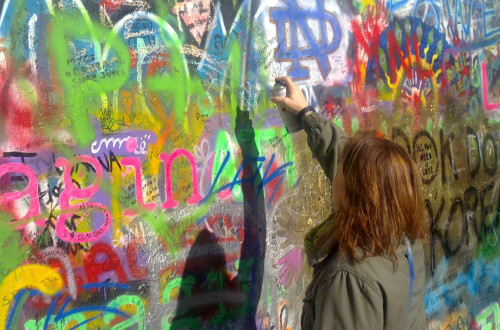 Zenska z rdecimi lasmi s sprejem ustvarja barvit grafit na ze obstojeci pisanih grafitih polni steni. 