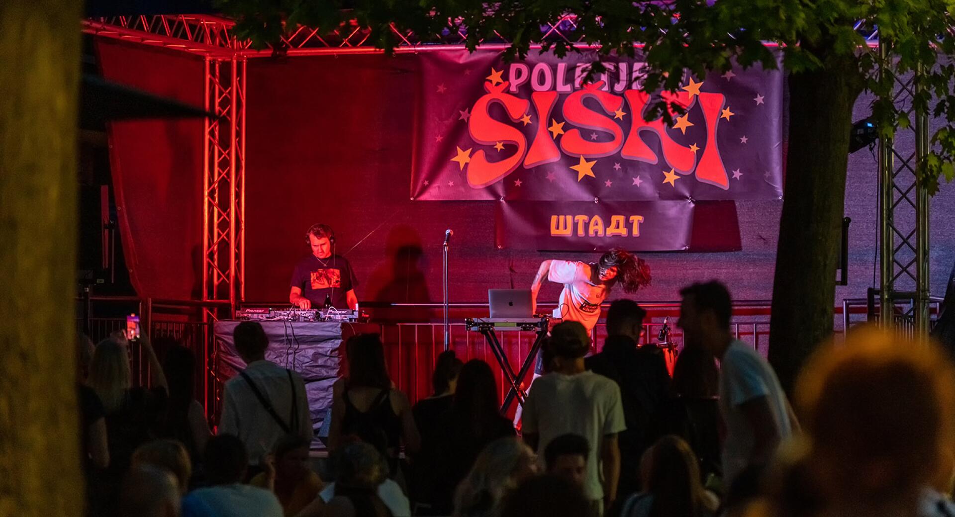 Večerni koncert, na odru DJ, pred njim občinstvo.