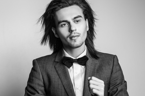 A black-and-white photograph of a man with long hair wearing a suit.