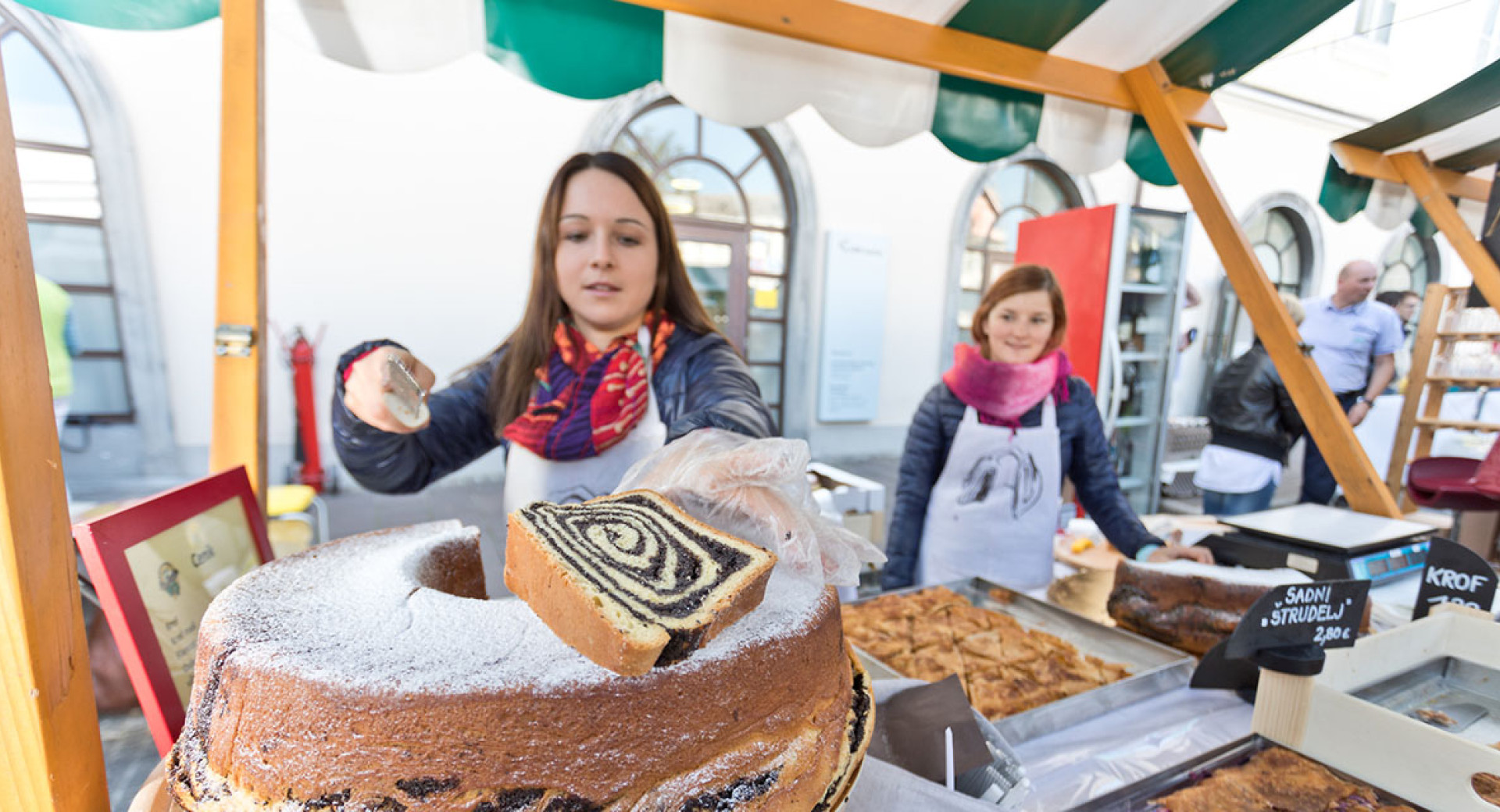 Prodajalka v roki s slovensko tradicionalno potico. V ozadju prodajalka.