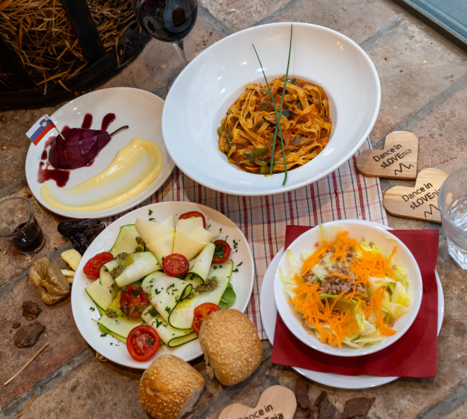 A rustic table set with four plates of various vegetarian dishes, two loaves of bread, and a glass of water, on a red-and-white checkered cloth.