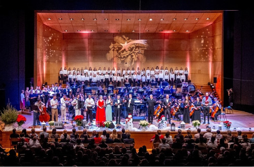 Orkester in zbor nastopata na odru v dvorani, pred njima sedi obcinstvo.