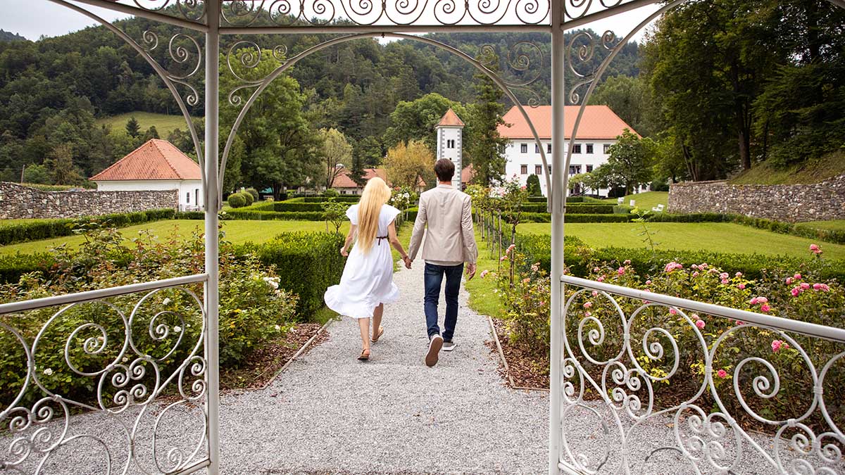 A park with a mansion in the background. A woman and a man holding hands, with the mansion in the background.