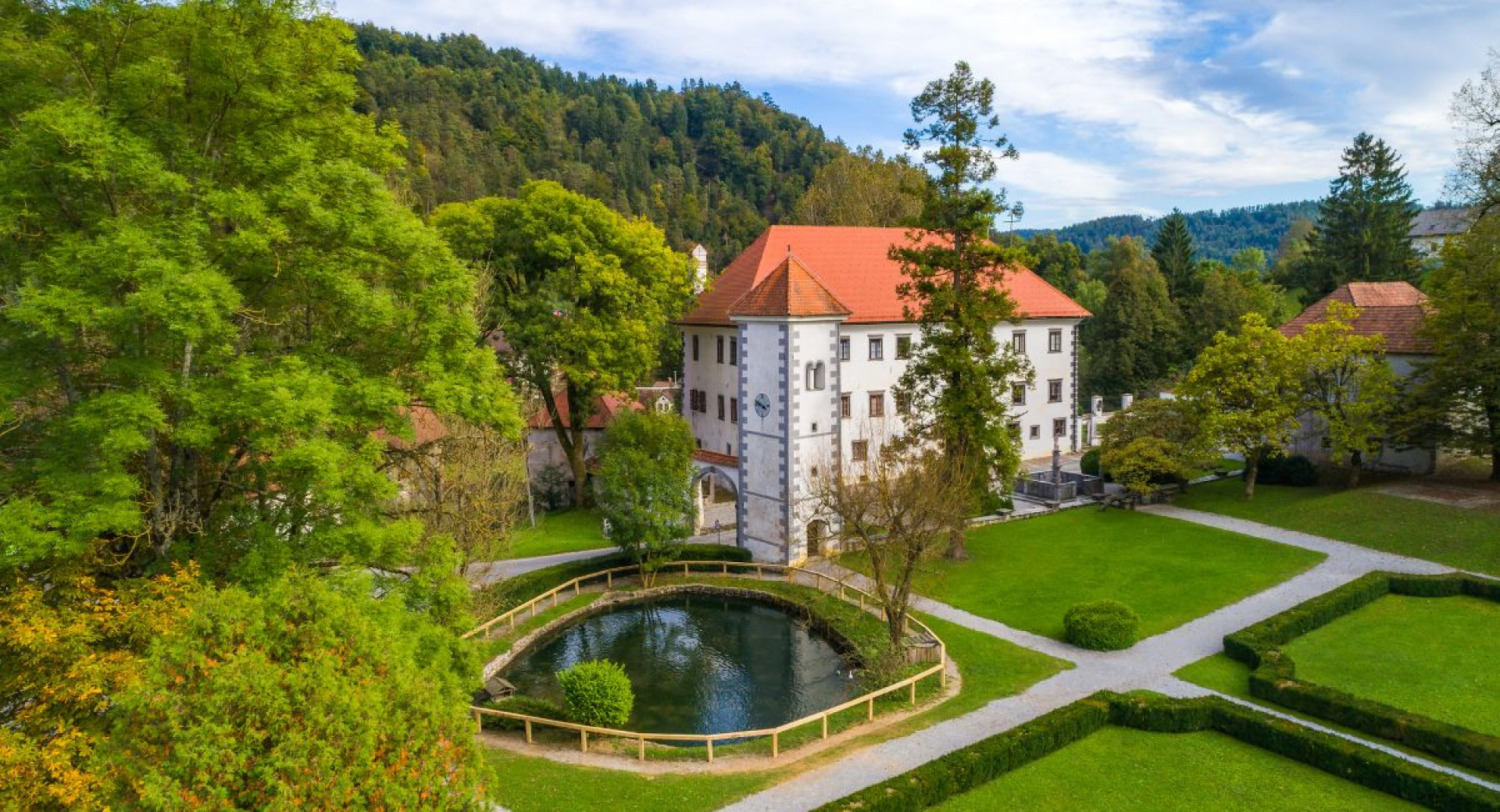 Graščina in urejen grajski vrt z bajerjem. Graščina z belo fasado in rdečo streho.