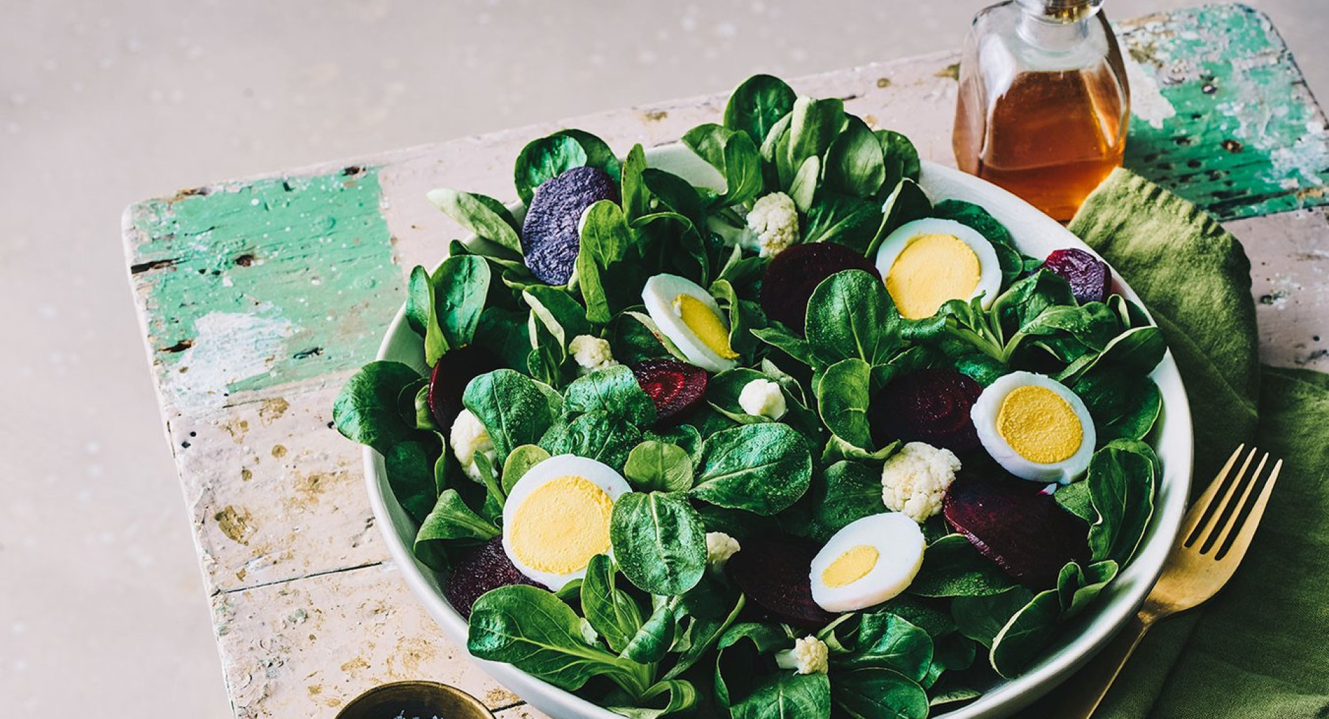 A bowl of dandelion salad with hard-boiled eggs on a wooden board, white background.