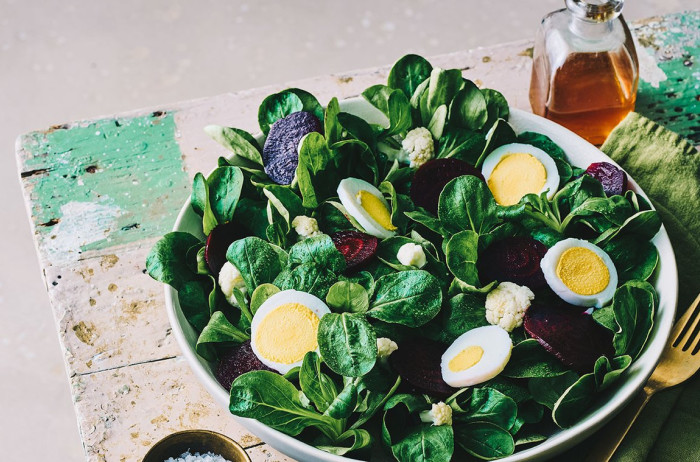 A bowl of dandelion salad with hard-boiled eggs on a wooden board, white background.