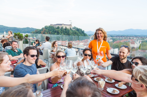 Ljudje nazdravljajo z vinom, v ozadju grad na hribu.