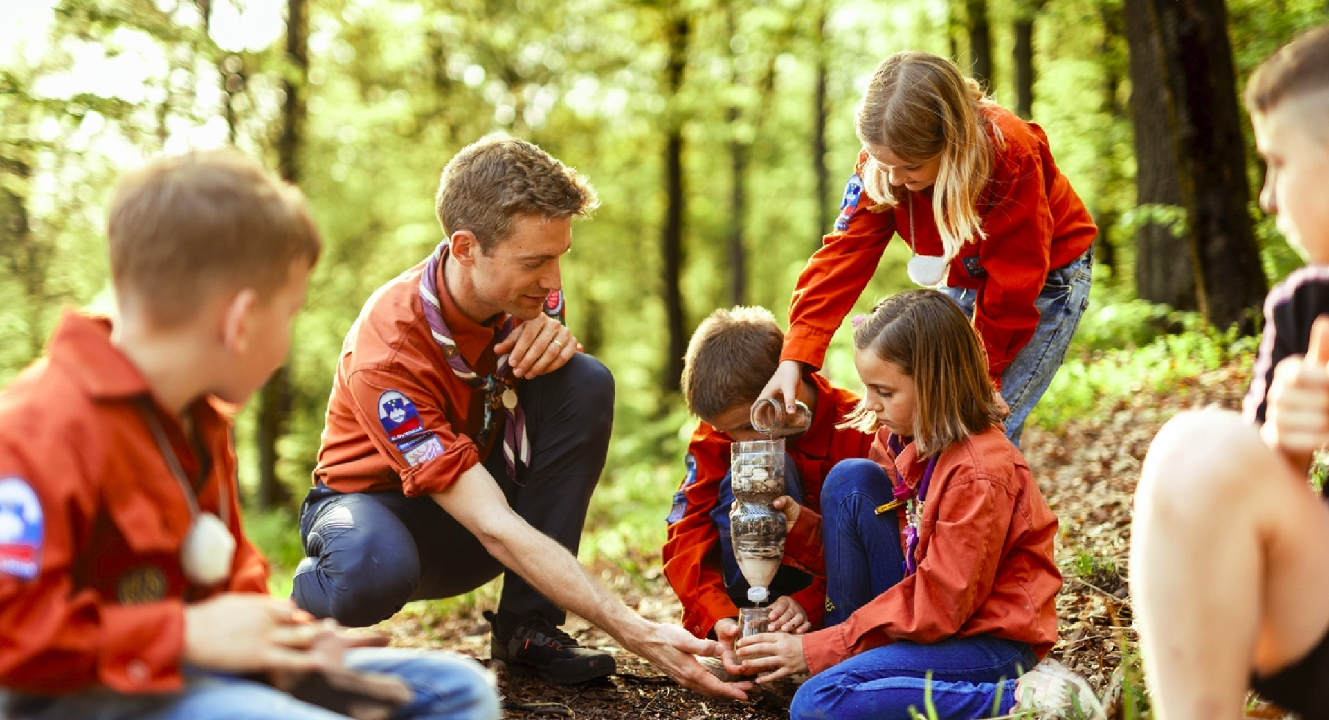 Skupina otrok in odraslega med dejavnostmi v gozdu.