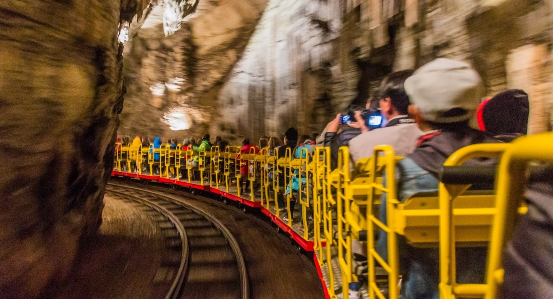 Visitors ride a small train through the stunning underground passages of Postojna Cave, surrounded by impressive rock formations.