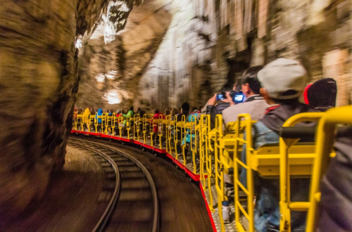 Visitors ride a small train through the stunning underground passages of Postojna Cave, surrounded by impressive rock formations.