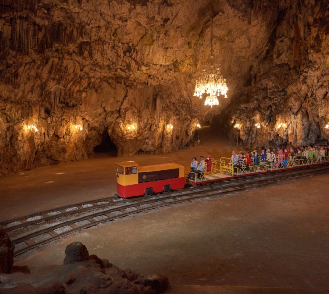 Visitors enjoy a scenic train ride through a vast, illuminated cavern inside Postojna Cave.