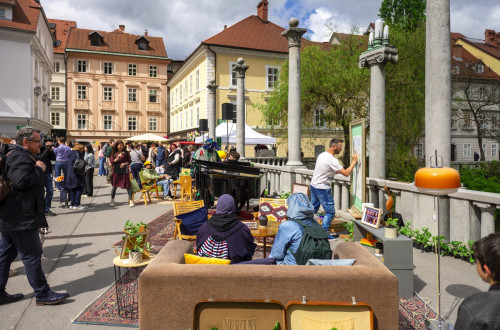 Dogajanje na prostem: obiskovalci sedijo na kavču, umetnik riše na platno, pianist igra na klavir ...