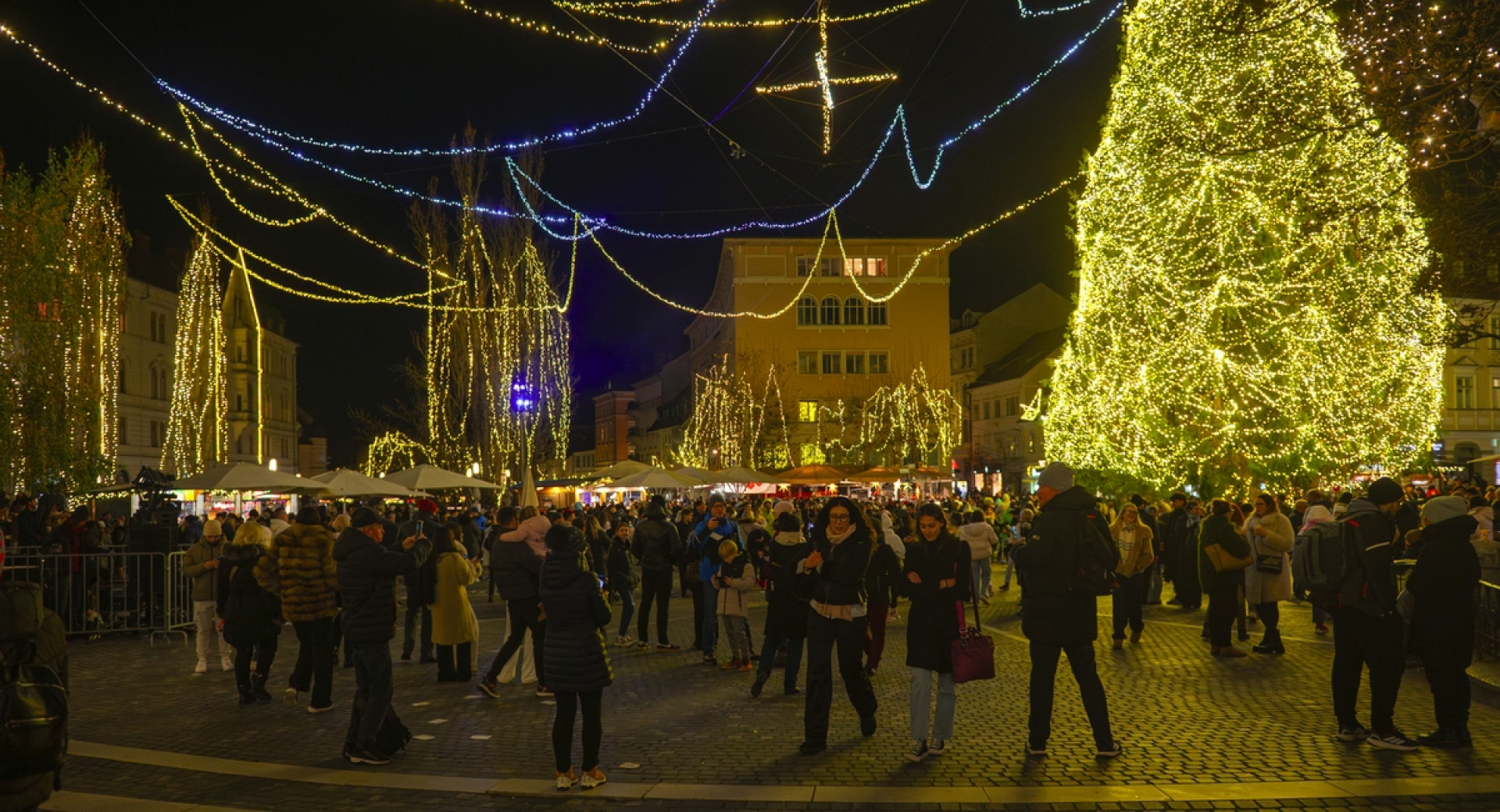 Številni obiskovalci na mestnem trgu z visoko okrašeno smreko.