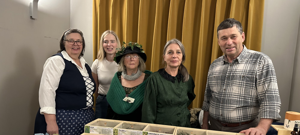 A group of five people is standing behind a table at a fair. Numerous wooden boxes with dried herbs and teas are displayed on the table.
