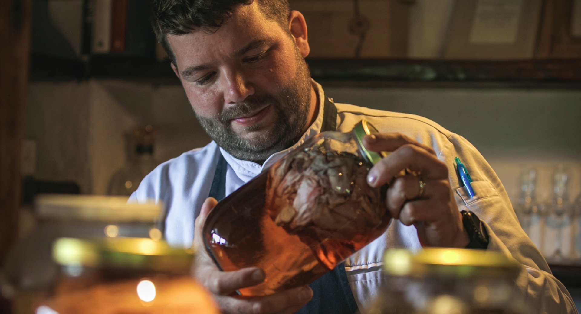 Luka Košir, cher restavracije Grič, drži v rokah velik kozarec z vložninami, pred njim druge, polne streklene posode.