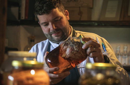 Luka Košir, cher restavracije Grič, drži v rokah velik kozarec z vložninami, pred njim druge, polne streklene posode.