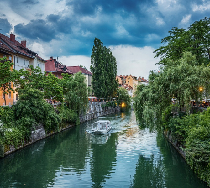Grüne Uferpromenaden der Stadt, während ein Boot auf dem Fluss dahingleitet.