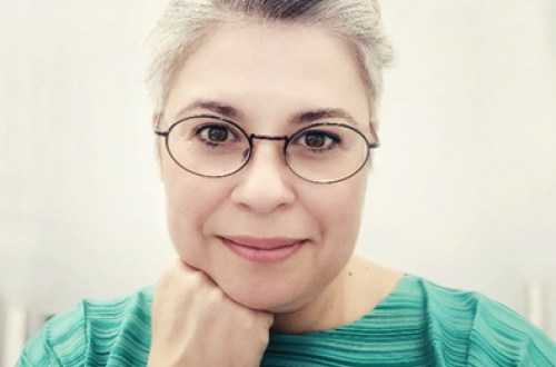 A blonde girl with glasses wearing a green T-shirt.