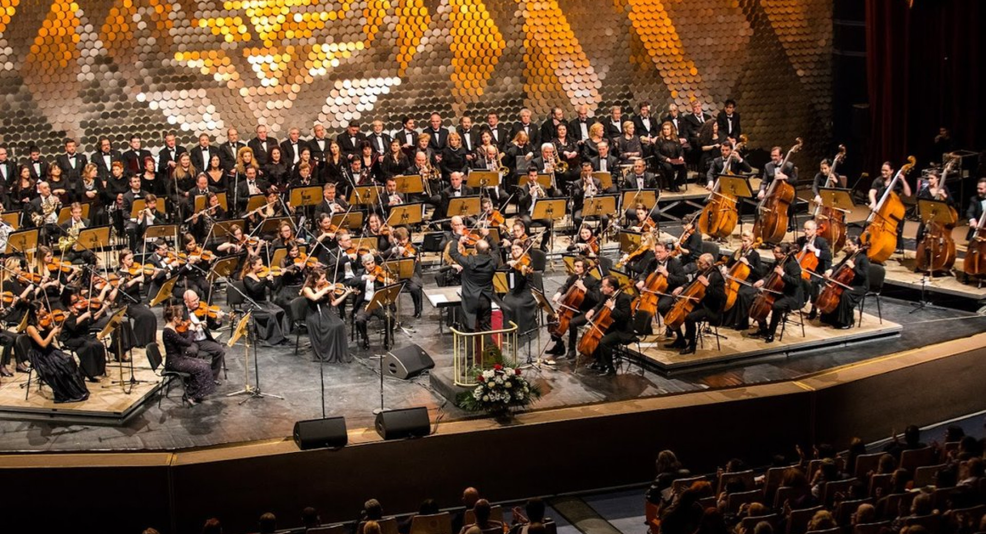 orkester na odru sredi nastopa, v ozadju zlata projekcija