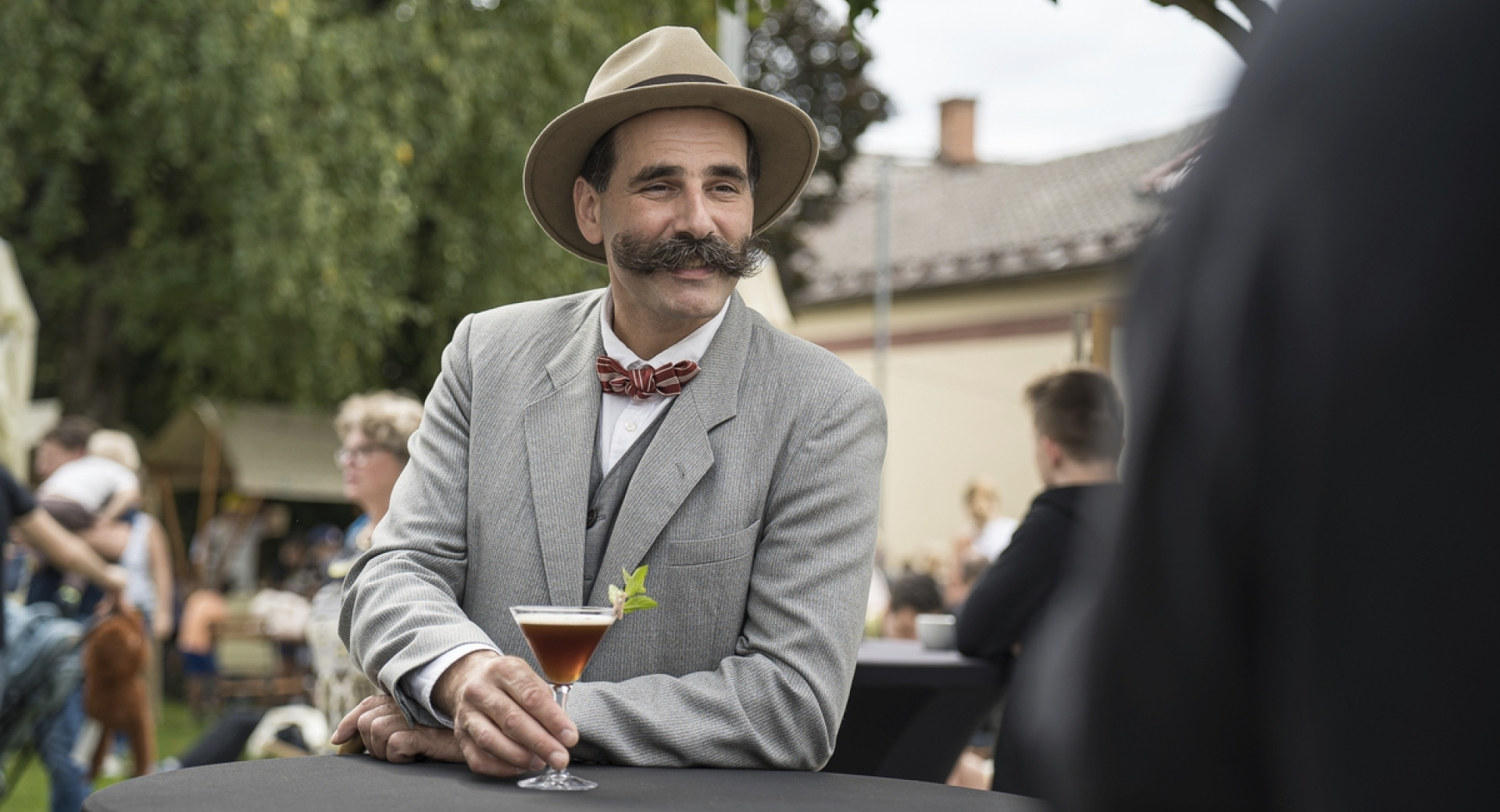 Oseba, preoblečena v pisatelja Ivana Cankarja s pijačo v roki.