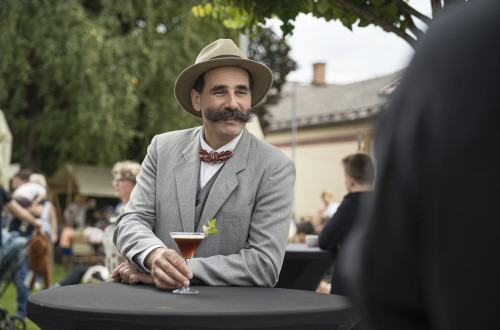 Oseba, preoblečena v pisatelja Ivana Cankarja s pijačo v roki.