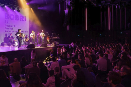 Koncert: glasbeniki na odru, pred njimi občinstvo.