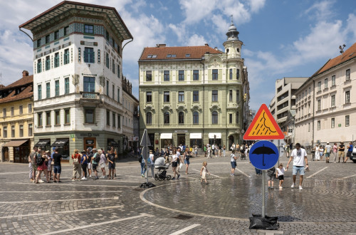 Trg sredi mesta, na njem ljudje in table z znakom za dežnik in dež.