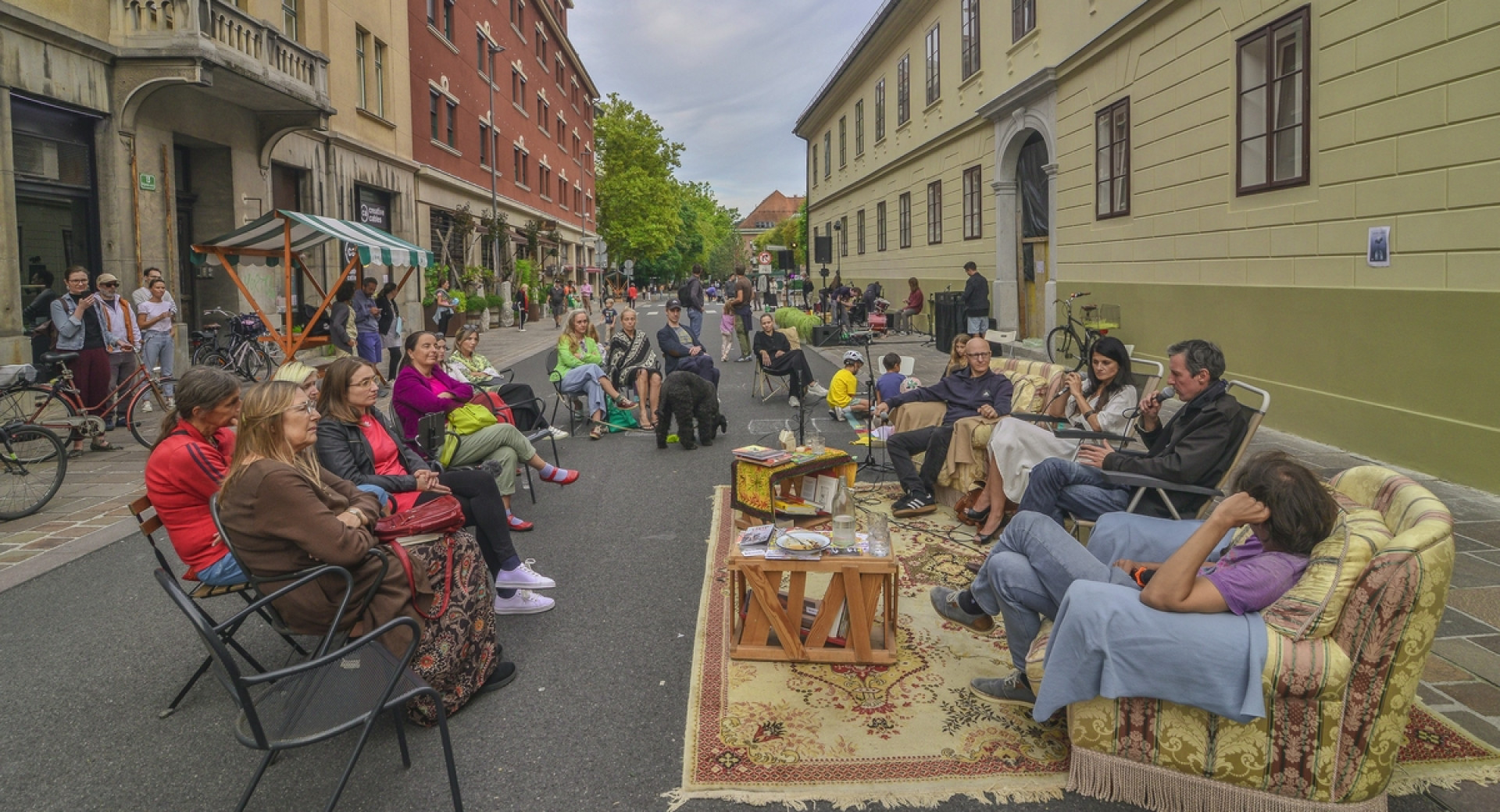 Ljudje sedijo v foteljih in na stolih sredi ulice.