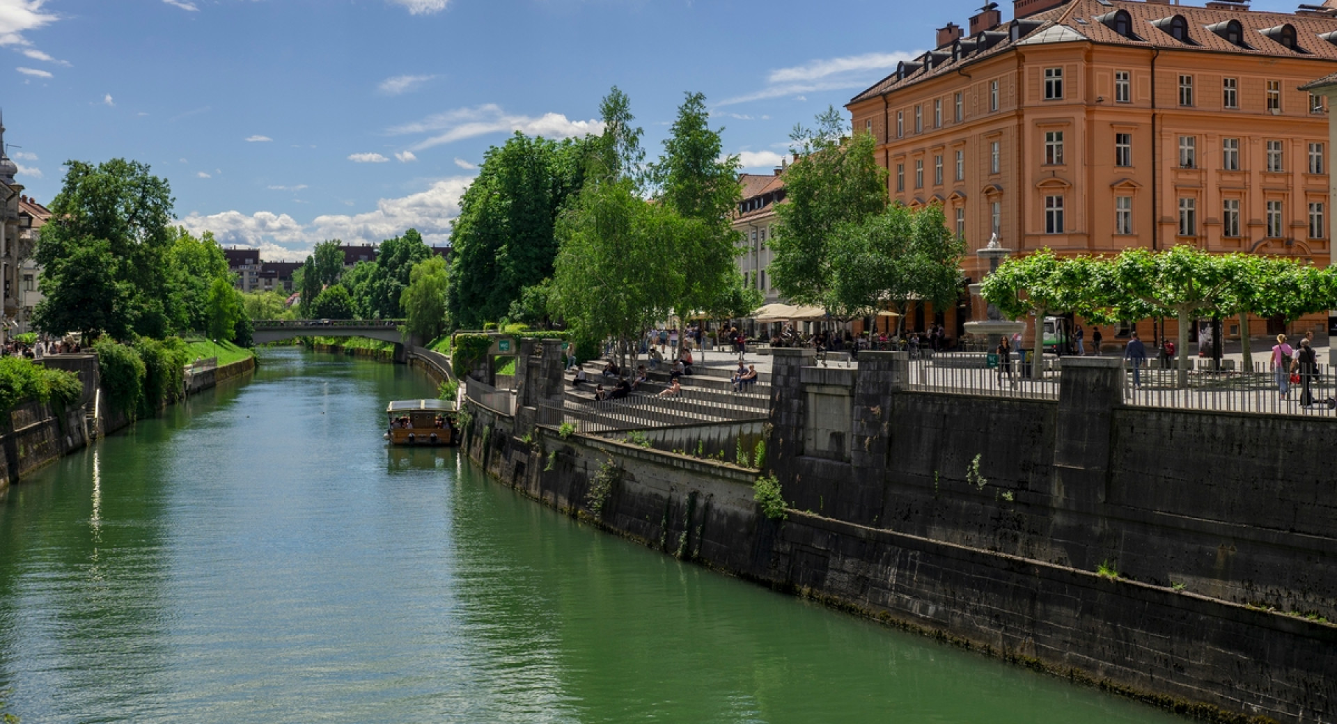 Reka Ljubljanica, na njej ladjica, ob njej nabrežje s stavbami.