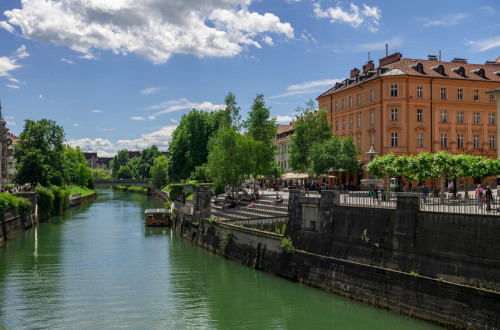 Reka Ljubljanica, na njej ladjica, ob njej nabrežje s stavbami.