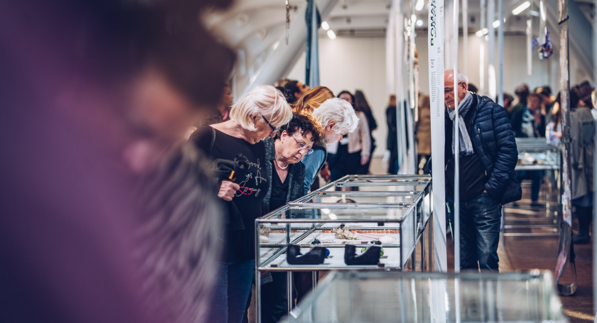 Obiskovalci se sklanjajo nad vitrinami z razstavljenim nakitom.