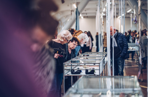 Obiskovalci se sklanjajo nad vitrinami z razstavljenim nakitom.