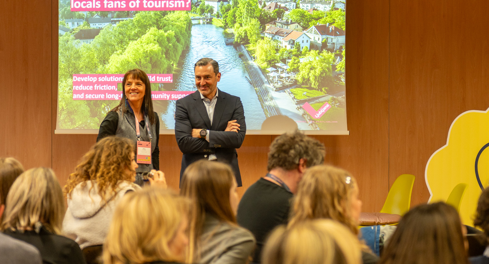 Dve osebi stojita na odru, pred njima občinstvo.