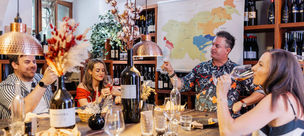 Menschen sitzen am Tisch und machen eine Weinprobe. Auf dem Tisch stehen Gläser und Weinflaschen.