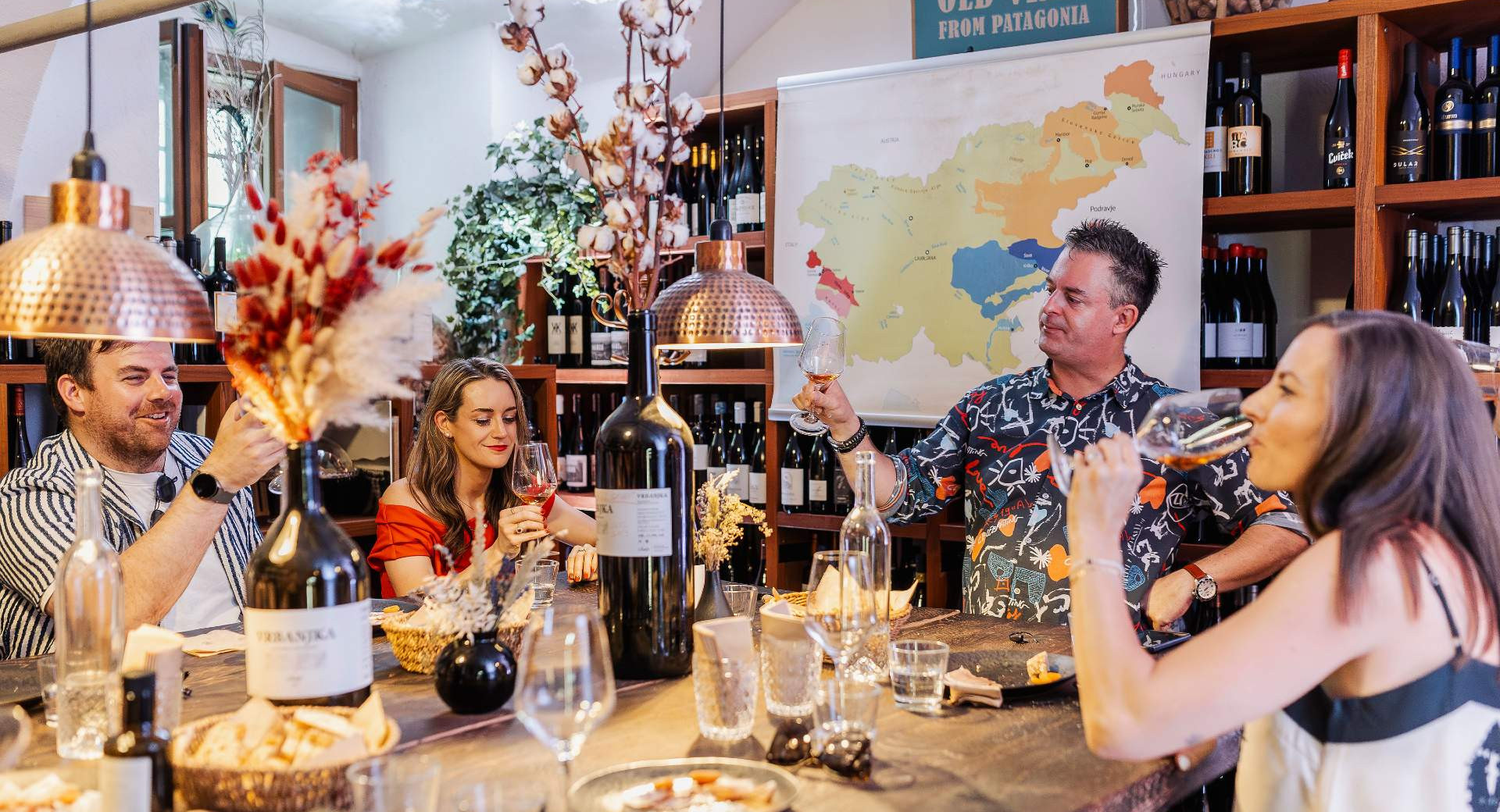 Menschen sitzen am Tisch und machen eine Weinprobe. Auf dem Tisch stehen Gläser und Weinflaschen.