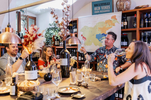 People are sitting at a table and tasting wine. There are glasses and bottles of wine on the table.