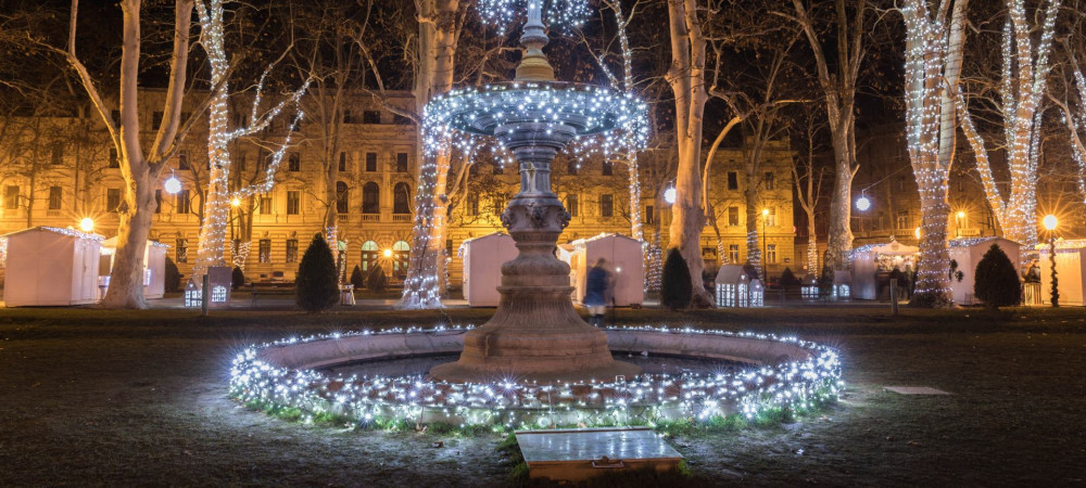 Una fontana nel mezzo del parco al crepuscolo, decorata con luci natalizie.