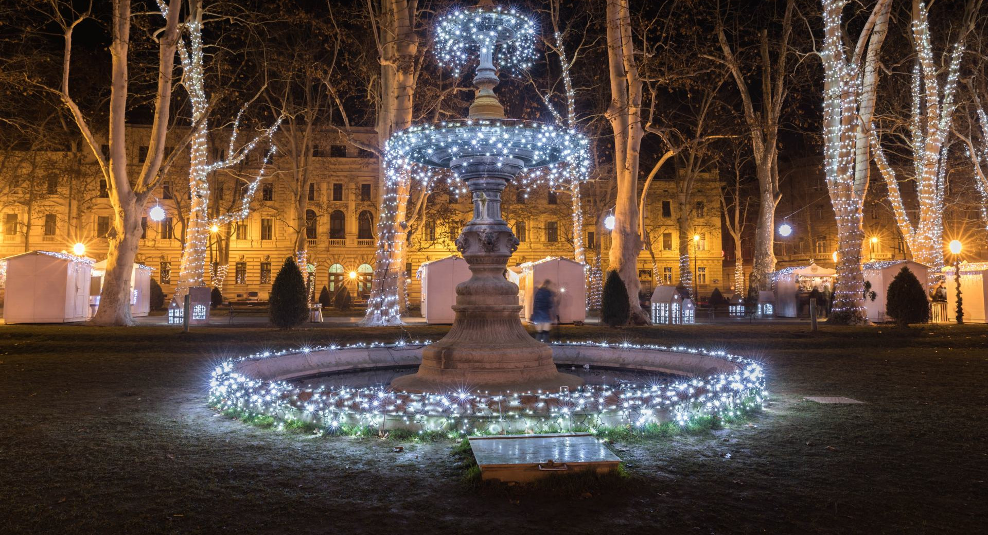 Una fontana nel mezzo del parco al crepuscolo, decorata con luci natalizie.