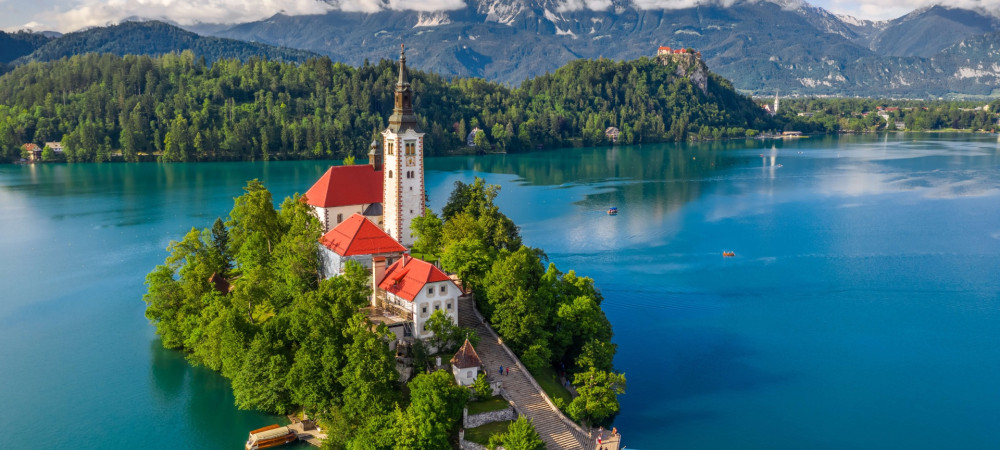 A small island with a church in the middle of a lake, with mountains in the background.