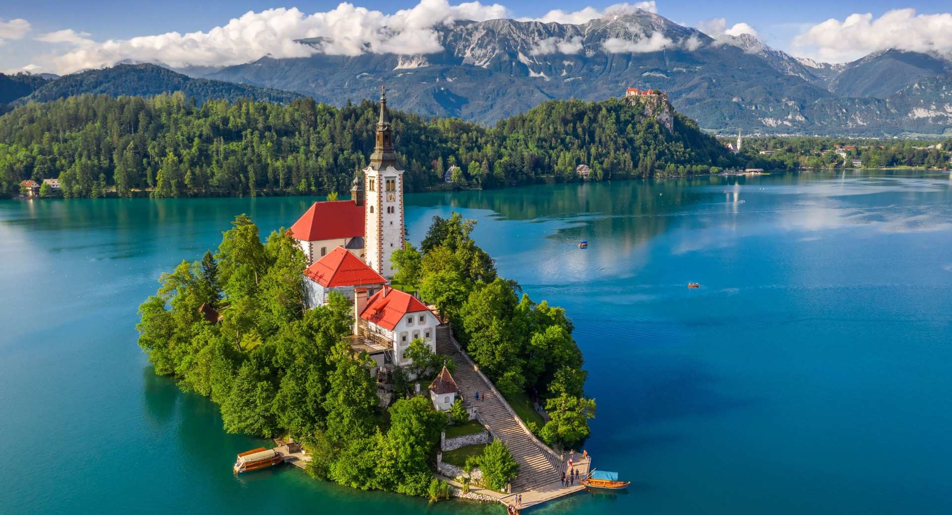 A small island with a church in the middle of a lake, with mountains in the background.