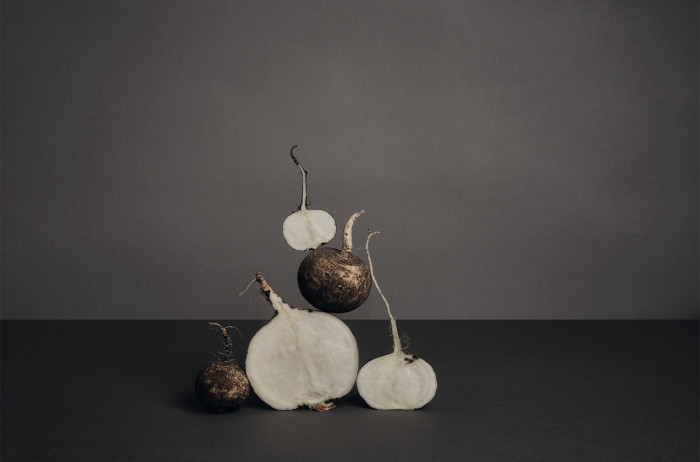 A whole and halved radish arranged in a pyramid shape. Black background, gray backdrop.