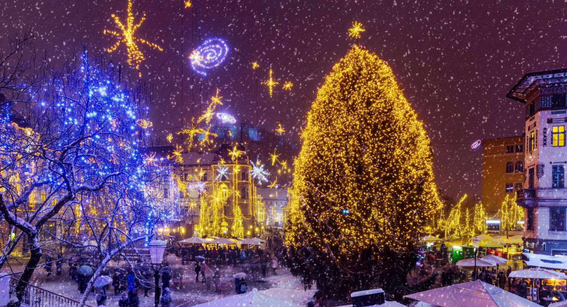 Sapin de Noël illuminé au milieu de la place enneigée.